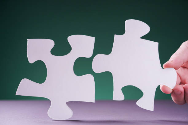 istock Hand holding piece of white puzzle on green background. 1202103713