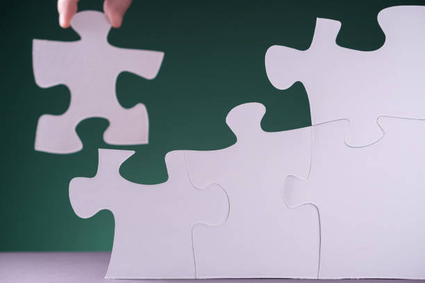 istock Hand holding piece of white puzzle on green background. 1202103720