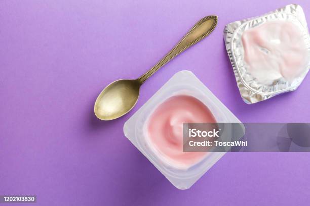 Healthy Strawberry Fruit Flavored Yoghurt With Natural Coloring In Plastic Cup Isolated On Purple Background With Small Spoon And Foil Lid Stock Photo - Download Image Now