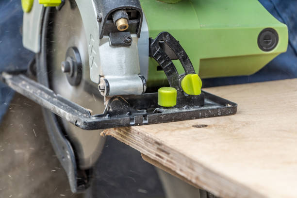 istock Man cuts a plywood plate using a green electric circular saw tool with yellow chips on a work bench 1202104029