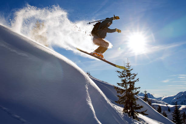 sciatore libero che fa un grande salto spruzzando neve fresca in polvere in una limpida giornata invernale soleggiata - european alps cold mountain range clear sky foto e immagini stock