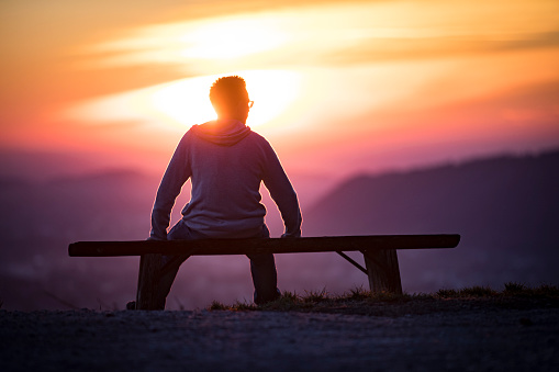 Young Adult Man Relaxing on Bench and Watching Landscape During Sunset.