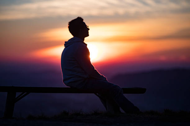 istock Young Adult Man Sitting on a Bench During Sunset 1202105274