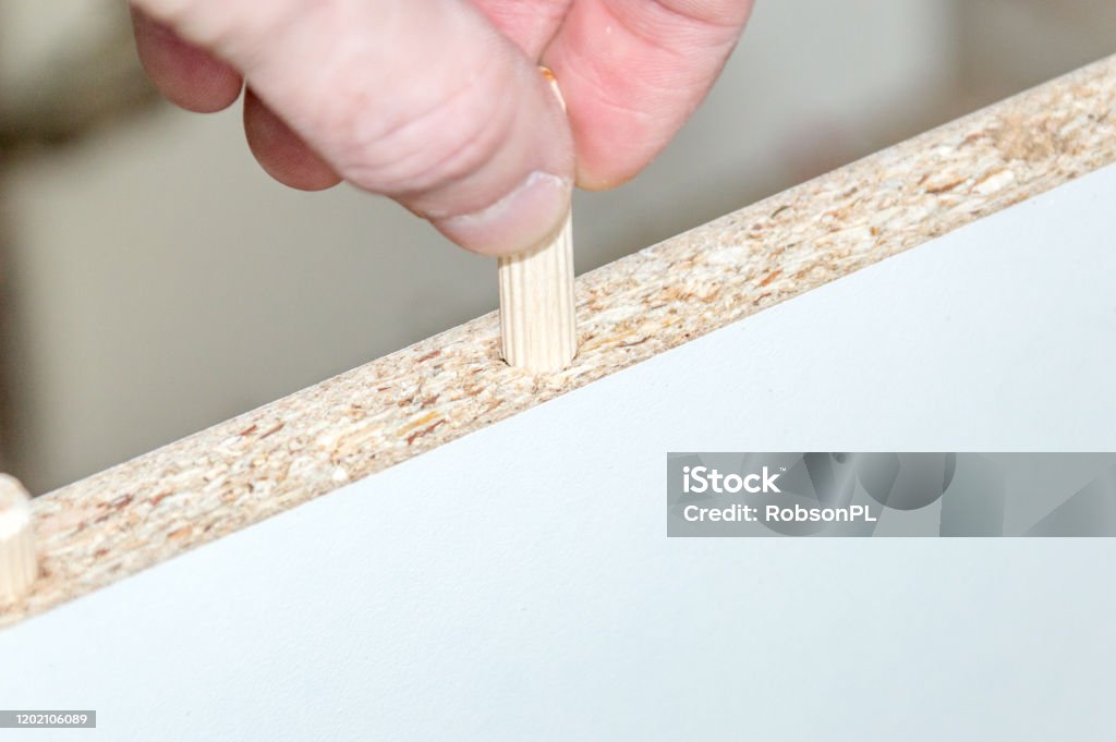 Inserting a wooden dowel into the hole in board chipboard. Furniture Stock Photo