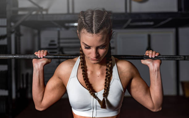 giovane ragazza muscolosa forte sudata con grandi muscoli che tengono il bilanciere dietro la testa preparandosi e concentrandosi per l'allenamento duro squats con pesi pesanti in palestra da vicino - crouching barbell weightlifting weight training foto e immagini stock