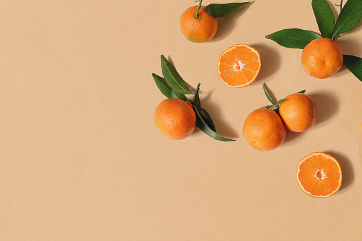 Styled stock photo. Decorative summer fruit composition. Whole and sliced orange tangerines, citrus fruit and leaves isolated on orange table background. Food pattern. Empty space. Flat lay, top view.