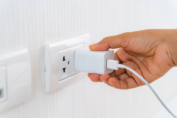 istock Woman's Hand Inserting Electrical Power Cord Plug into Receptacle on wall outlet. 1202119069