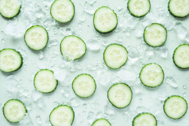 Pattern with freshly cut cucumber slices and ice cubes on green background stock photo