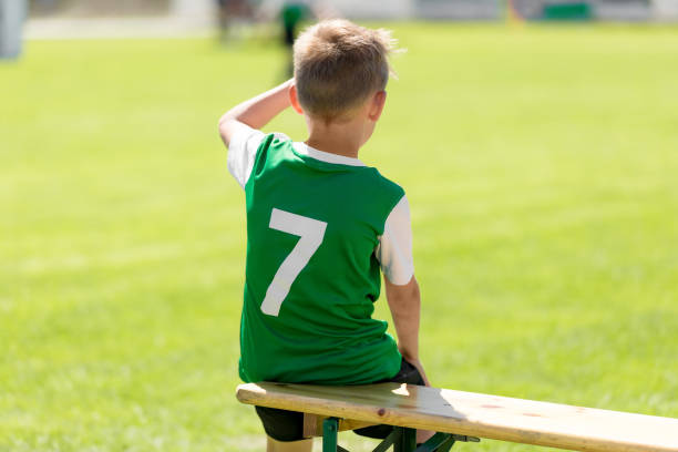 chłopiec z piłki nożnej w koszulce grean siedzącej na drewnianej ławce - soccer bench soccer player sport zdjęcia i obrazy z banku zdjęć