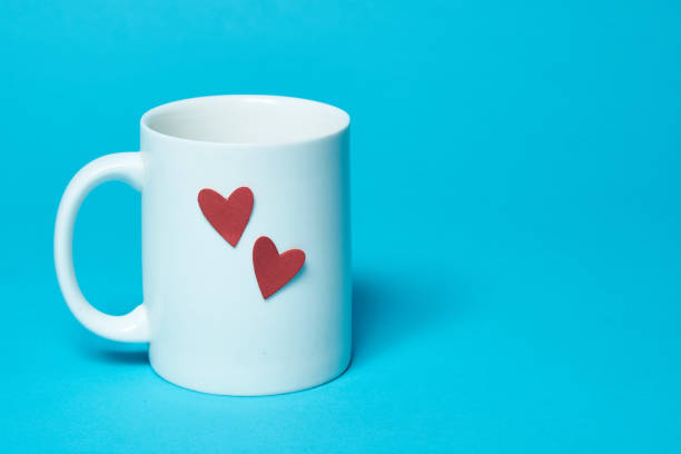 istock White ceramic cup isolated on a blue background. On a cup are two red paper hearts. Free space for text. Simplicity 1202132594