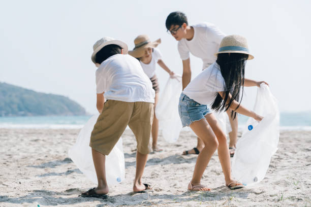 bénévole asiatique de famille ramassant une bouteille en plastique sur une plage avec une mer pour protéger un environnement - rescue can photos et images de collection