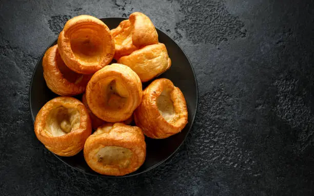 Traditional English Yorkshire pudding side dish on black plate and background.
