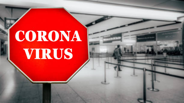 Coronavirus written on stop sign with passengers arriving at passport control within generic airport
