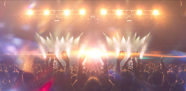 Front view of a concert stage with unrecognizable people silhouettes clapping and raising hands