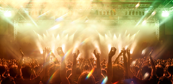 Front view of a concert stage with unrecognizable people silhouettes clapping and raising hands