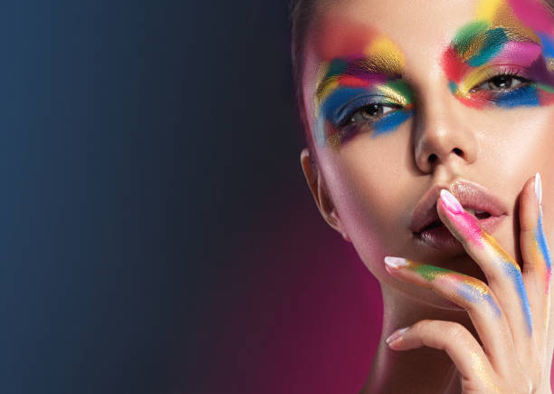 istock Bright, extravagant, multi colored makeup on the young pretty face. Makeup art, manicure and cosmetic products. 1202143388