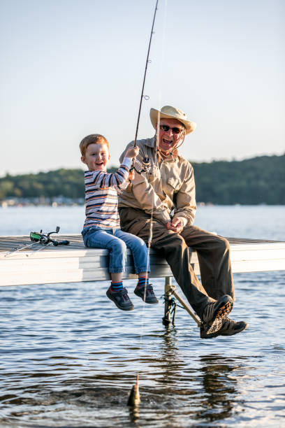 grand-père et petit-fils pêchant au coucher du soleil en été - fishing lake grandfather grandson photos et images de collection