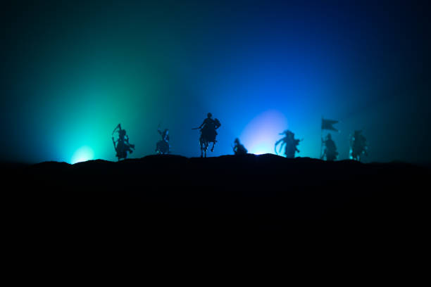 istock Medieval battle scene with cavalry and infantry. Silhouettes of figures as separate objects, fight between warriors on dark toned foggy background. Night scene. 1202153908
