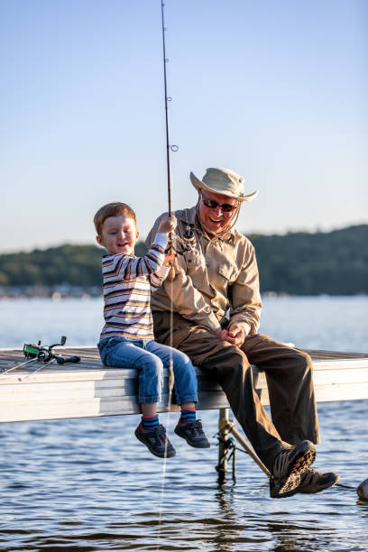 grand-père et petit-fils pêchant au coucher du soleil en été - fishing lake grandfather grandson photos et images de collection
