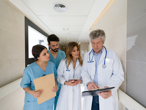 Senior doctor talking to his team of interns while pointing something on clipboard at the hospital  - healthcare concepts