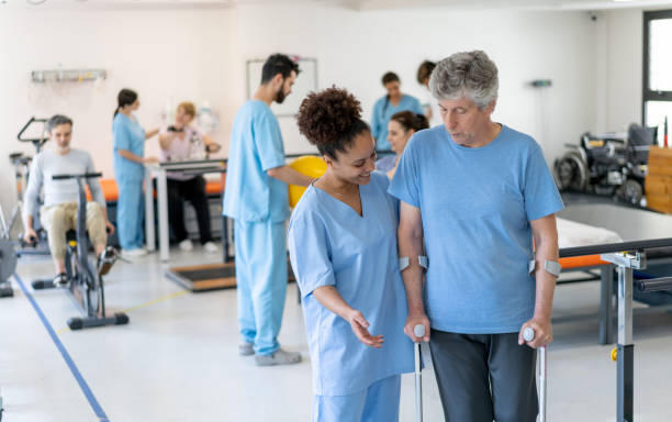 istock Black cheerful therapist assisting senior man walking with crutches at physical therapy 1202157433