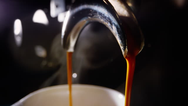 Close-Up Shot of Espresso Pouring from both Sides of an Espresso Maker Spout and into a Small Coffee Mug in a Coffee Shop