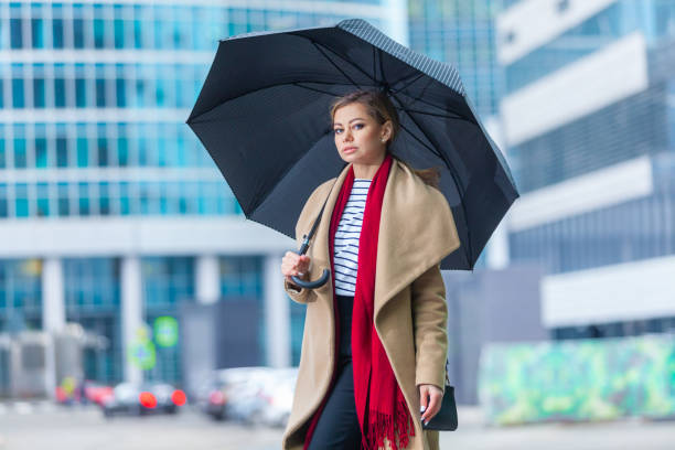 雨。見事なブルネットの女の子のアウトドアライフスタイルファッションの肖像画。街の通りを歩く。買い物に行く。●スタイリッシュな白いフィットコート、赤いネックスカーフ、ブラッ� - neckscarf ストックフォトと画像