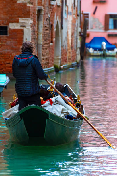 곤돌라/ 오스만은 노를 젓는 관광객/ 사람들과 함께 곤돌라에 서 있습니다. 물 운하 채널에 오래 된 벽돌 벽 고딕 양식의 베네치아 건물에 의해 인기 있는 낭만적 인 관광 보트 를 타고. - rowboat nautical vessel stern wood 뉴스 사진 이미지