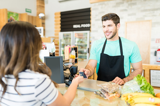 Smiling male cashier receiving payment through credit card in supermarket