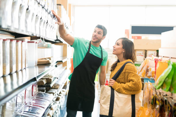 Salesman Assisting Customer In Buying At Store Confident male owner showing various food products on shelf to female consumer in store salesman stock pictures, royalty-free photos & images