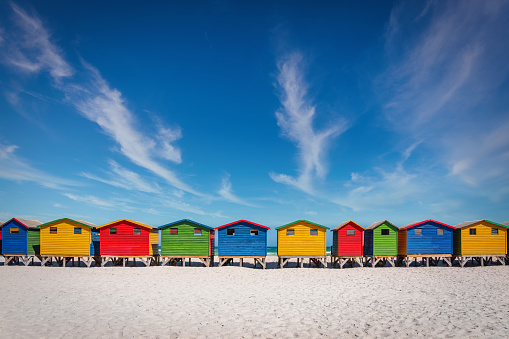 The famous and colorful iconic Muizenberg Beach Huts in a row under blue summer skyscape. Muizenberg Beach, Cape Town, South Africa, Africa.