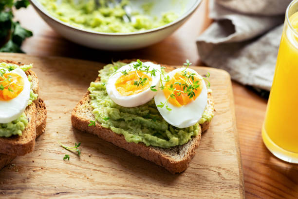 Toast with avocado and boiled egg Toast with avocado and boiled egg garnished with micro greens on a wooden table. Healthy breakfast food boiled egg photos stock pictures, royalty-free photos & images