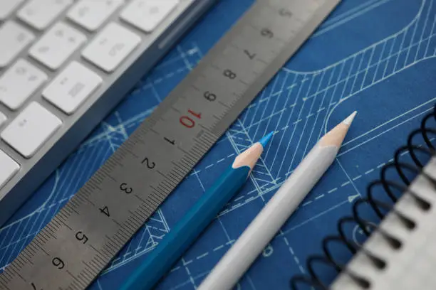 Photo of Drawing tools and computer keyboard lying over blueprint paper