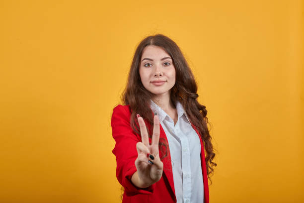 istock Brunette young woman showing victory gesture, looking at camera, smiling 1202195029