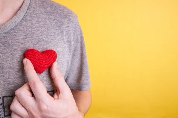 мужчина держит в руках символ сердца. изолирова�ны на желтом фоне. - day expressing positivity clothing desire стоковые фото и изображения