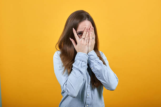 istock Attractive woman covered face with hands, looking at camera through fingers 1202208263