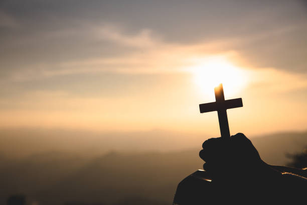 istock human hands praying to the GOD while holding a crucifix symbol with bright sunbeam. 1202210326