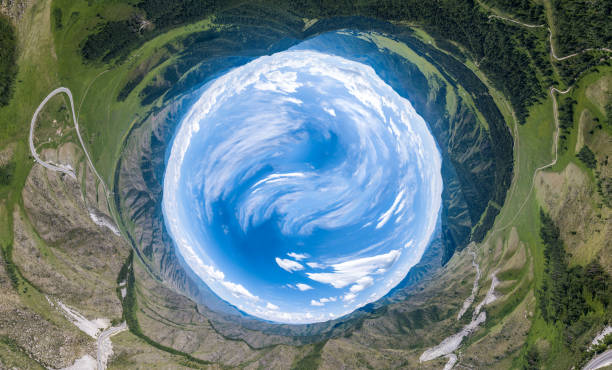 360 degree panoramic image of an abstract world turned inside out with green meadows around an oval sky with clouds in Chike-Taman pass in the Altai mountains. View from the earth to the sky or space.