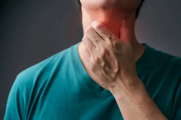 Photo of Unhappy Asian man using his hand touching on his neck Suffering From Gland Inflammation. Adult man feels bad on a sore throat and sick from cold, flu. Throat pain, sickness, healthcare, and medical concept.