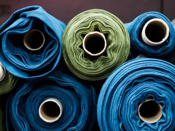 Photo of Blue and green rolls of knitted fabric. Woven factory or warehouse