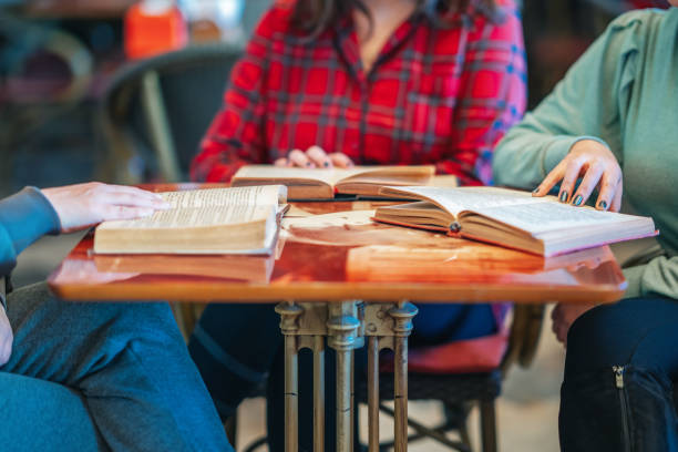 istock Three Intellectual women sitting and reading books in library or cafe. 1202214895