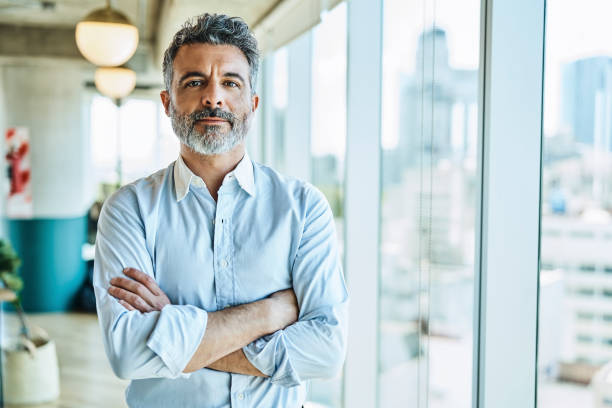 Confident businessman with arms crossed in office Portrait of confident mature businessman. Male entrepreneur is standing with arms crossed. He is at coworking office. 45 49 years stock pictures, royalty-free photos & images