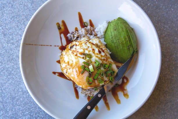 Healthy breakfast served on a white plate including fried egg, rice, avocado and sauce, scallions on a top. Restaurant brunch concert. Eating out.