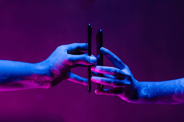 Sharing energy with wireless battery charging between two smart phones Two people sharing their battery power thanks to wireless charging from one mobile phone to the other. Shot in a studio environment with a futuristic neon lighting. two objects photos stock pictures, royalty-free photos & images