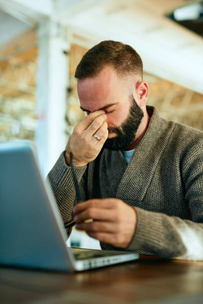 istock Young bearded man in a cafe suffering from headache after working on laptop 1202220454