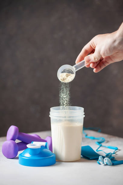 protein shake in bottle, powder,  and measuring tape on grey background. hand fills protein powder into bottle. sport food concept. - body building milk shake protein drink drink imagens e fotografias de stock