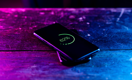 Two people sharing their battery power thanks to wireless charging from one mobile phone to the other. Shot in a studio environment with a futuristic neon lighting.