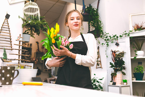 Portrait of a flower seller with tulips in hands. Young floristry works in a flower store