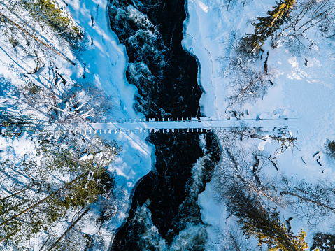 Aerial view of fast river with suspension foot bridge. Snow winter forest in Finland