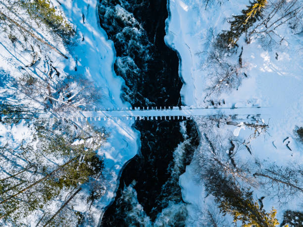 widok z lotu ptaka na szybką rzekę z wiszącym mostem na stopę. śnieżny las zimowy w finlandii - winter stream river snowing zdjęcia i obrazy z banku zdjęć